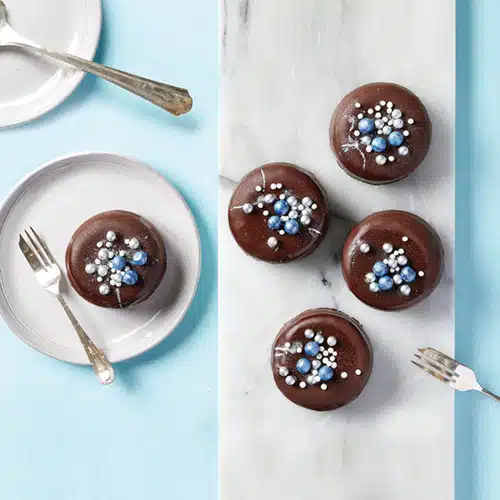 5 mini cheesecakes covered in chocolate, decorated with blue, white and silver sprinkles