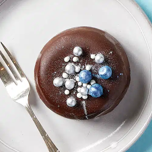 A mini cheesecake covered in chocolate, decorated with blue, white and silver sprinkles