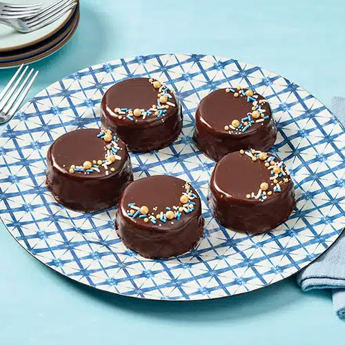 5 mini chocolate chip cheesecakes on a plate, decorated with gold, blue and white sprinkles