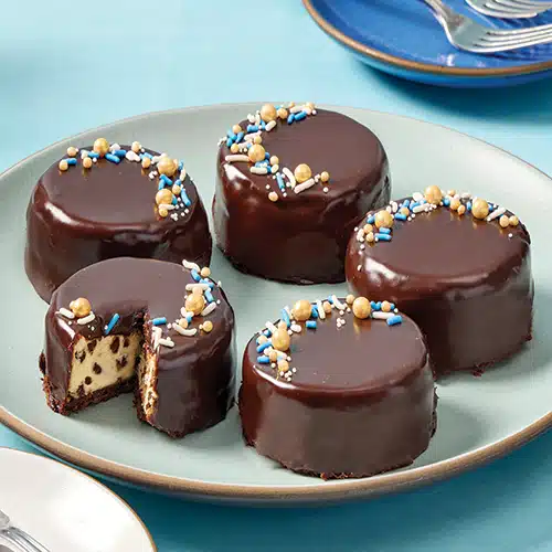 5 mini chocolate chip cheesecakes on a plate, decorated with gold, blue and white sprinkles