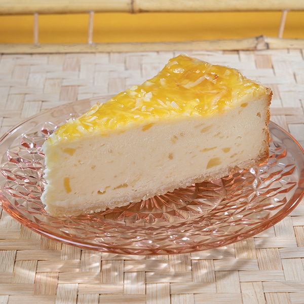 A slice of coconut cheesecake topped with pineapple glaze, on a pink plate.