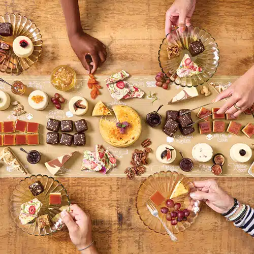 A cheesecake and dessert buffet on a table with guests plating their own desserts