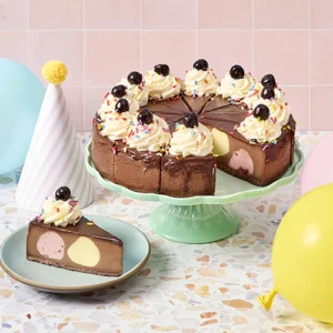 A cheesecake on a stand with balloons and a party hat
