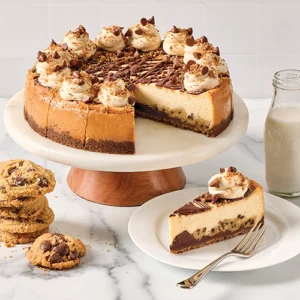 A cookie dough cheesecake on a cake stand with a slice removed