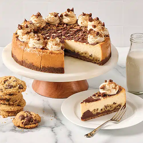 A cookie dough cheesecake on a cake stand with a slice removed