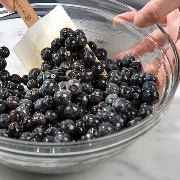 A bowl of fresh blueberry compote being stirred with a rubber spatula